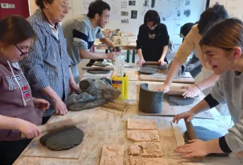 Elèves autour d'une table qui aplatissent de l'argile avec un rouleau