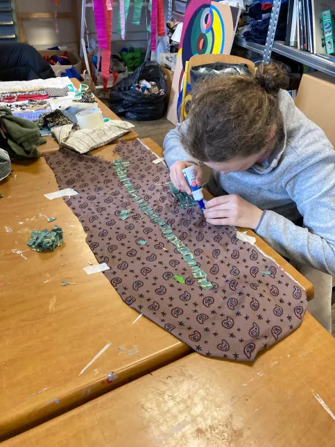 Elève colle un morceau de tissu sur son oeuvre textile