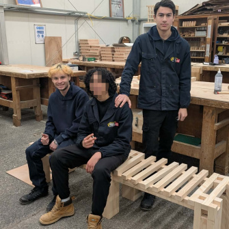 3 élèves en cap menuiserie assis sur le banc qu'ils ont fabriqué